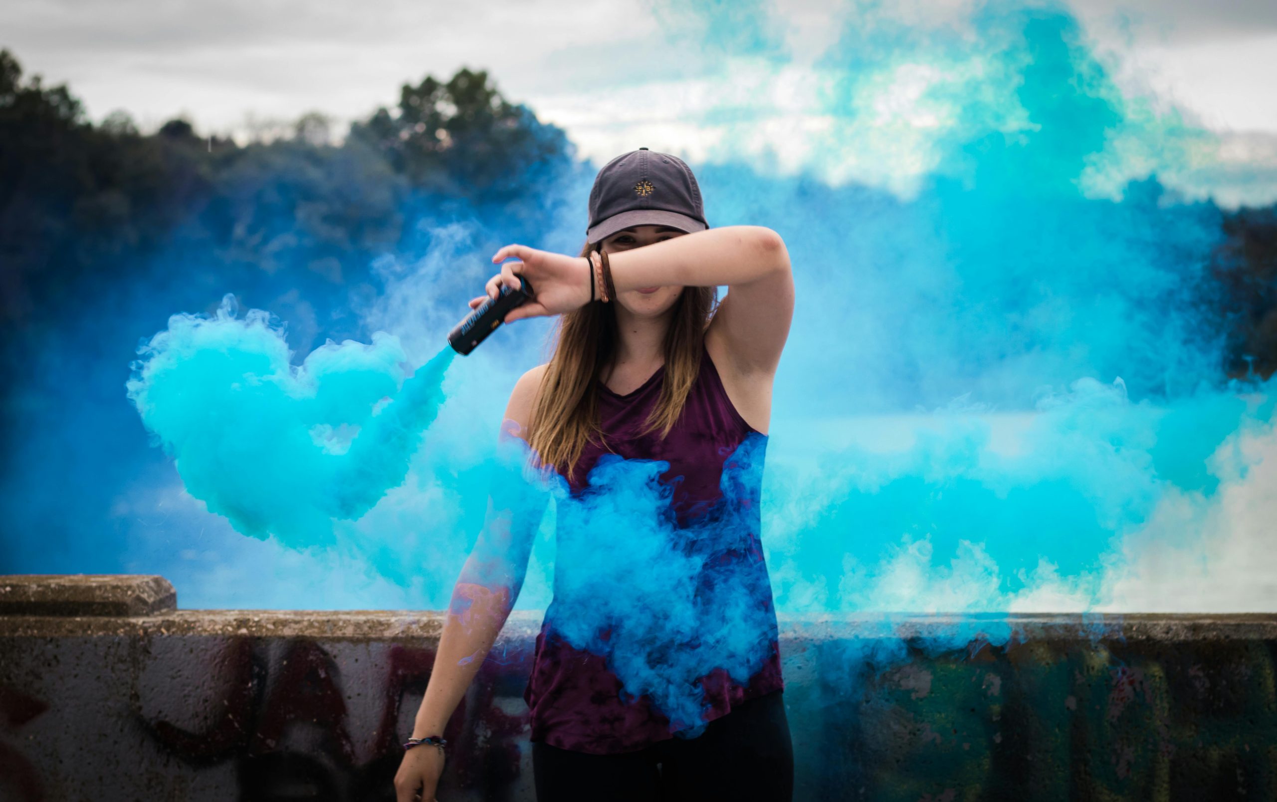 Home A stylish woman surrounded by bright blue smoke outdoors, creating a dynamic fashion statement.